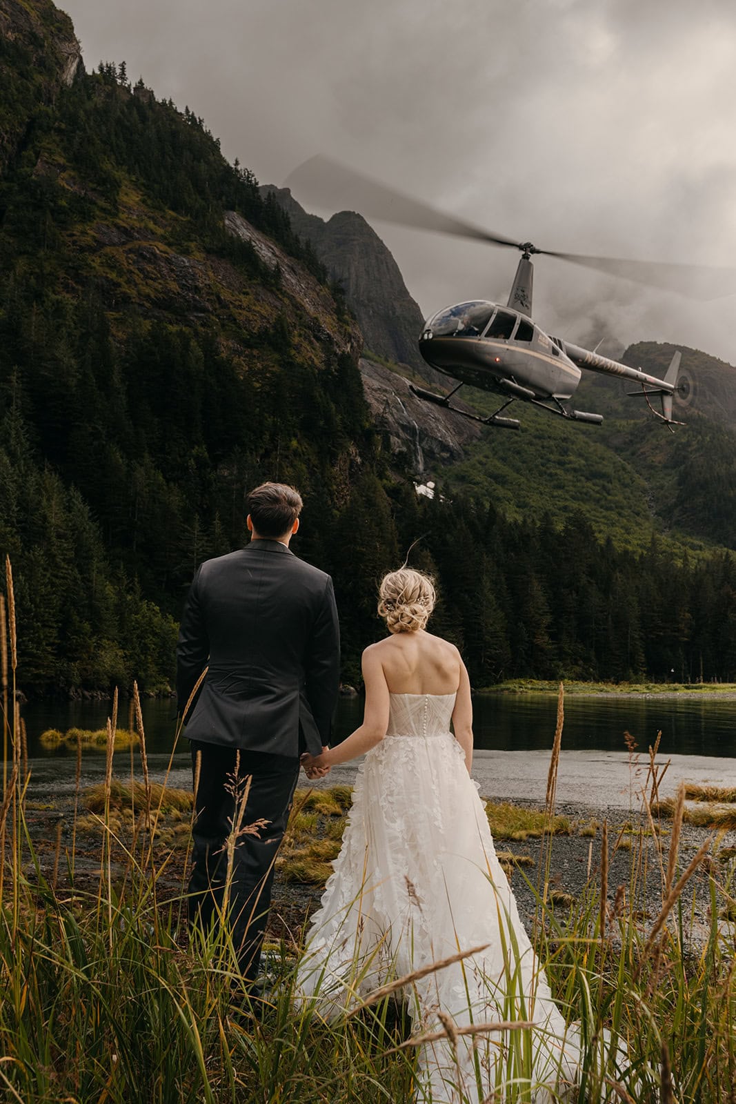A bride and groom watch as a helicopter flys away from them in Alaska.