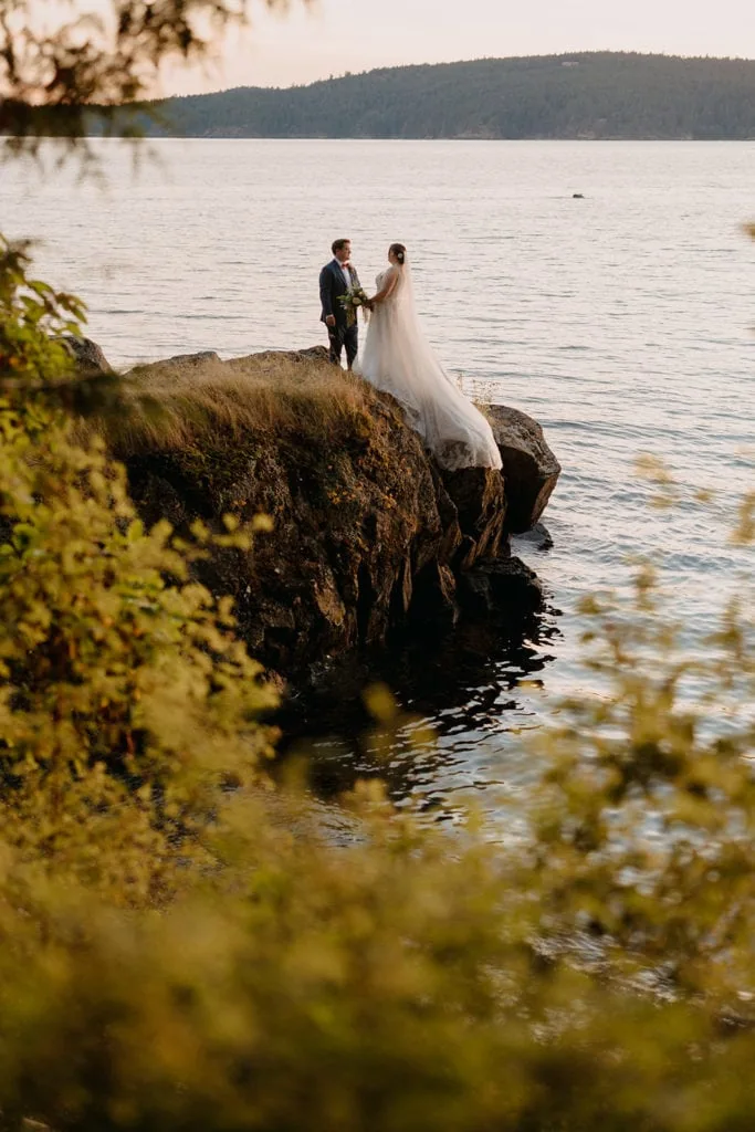 a couple overlooks the water as they hold hands.