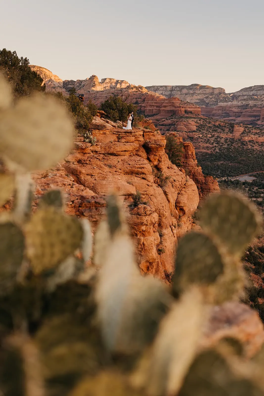 A bride and groom watches as the sun starts to rise over red rock cliffs.