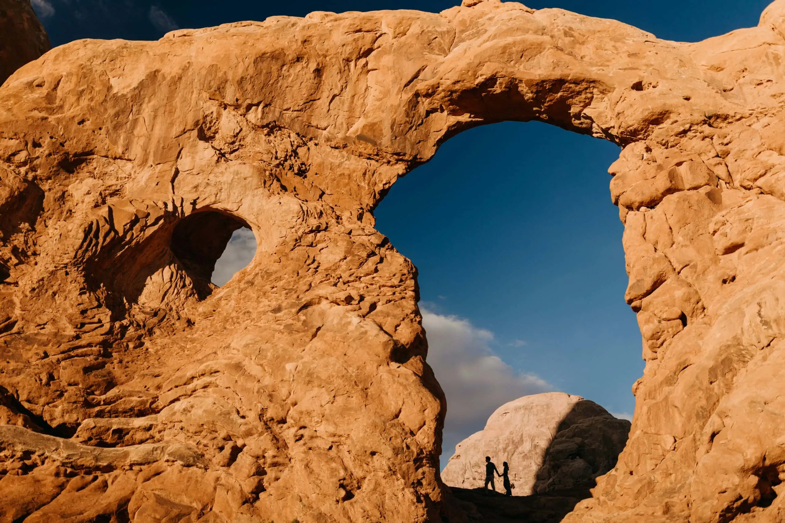 A couple explores an arch in Arches National Park.