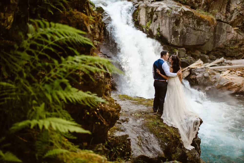 A couple shares a kiss while admiring a waterfall. 