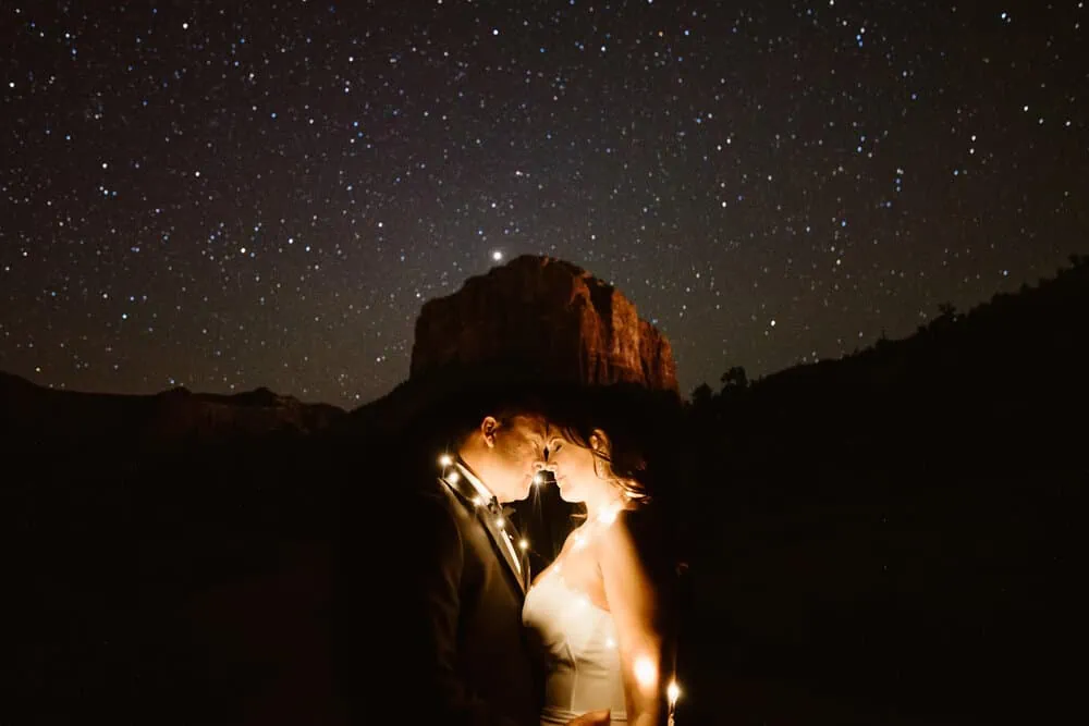 A bride and groom stand together, holding their foreheads close while the stars shine in the background.