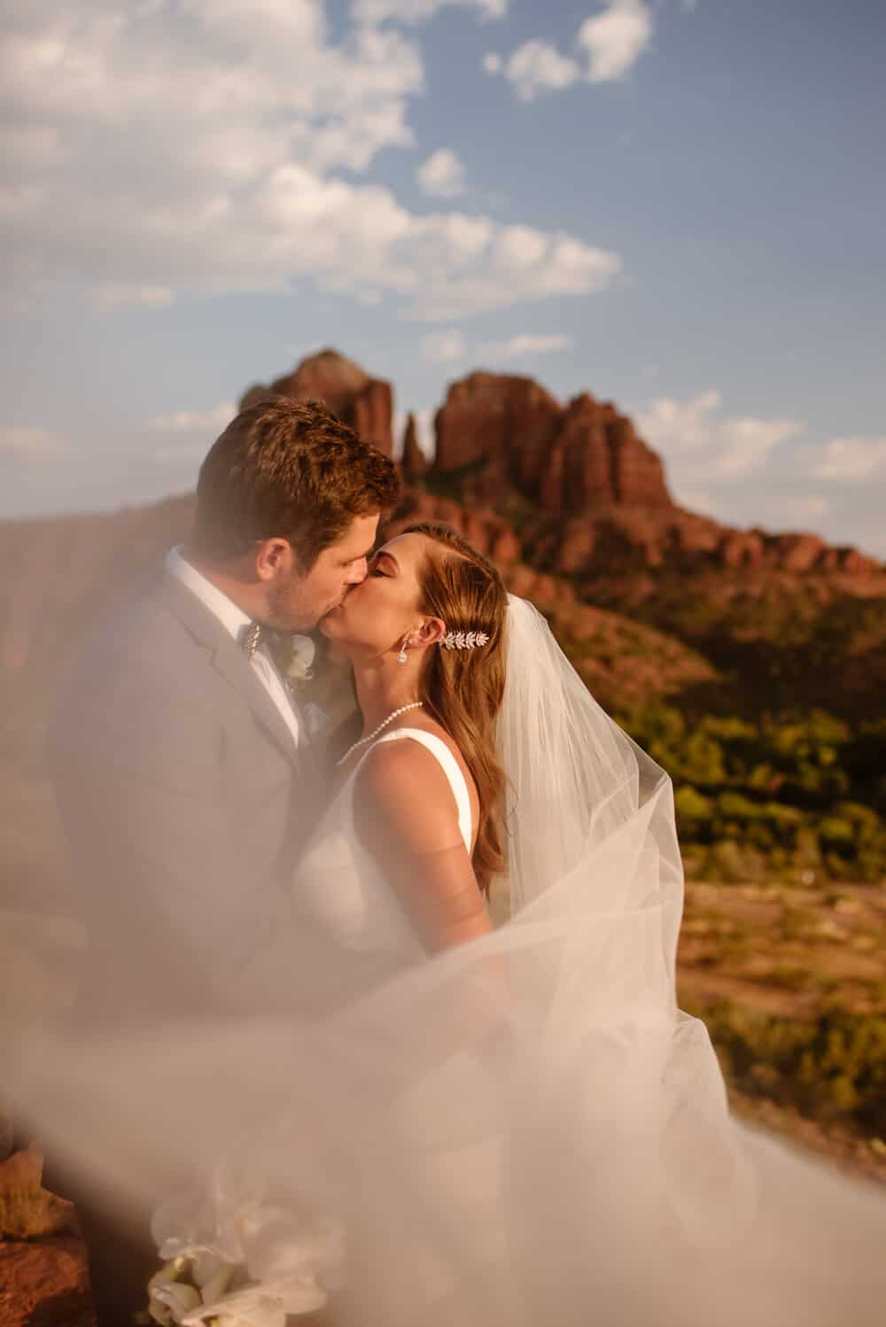 A bride and groom share a kiss with cathedral rock in the background.