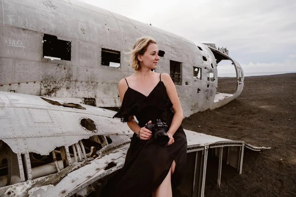 Portrait of a girl in a black dress sitting on a crashed plane. 