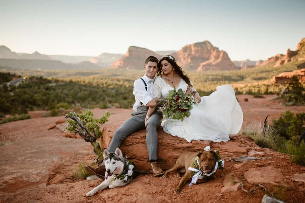 A couple sits at sunset in the desert with their two dogs.