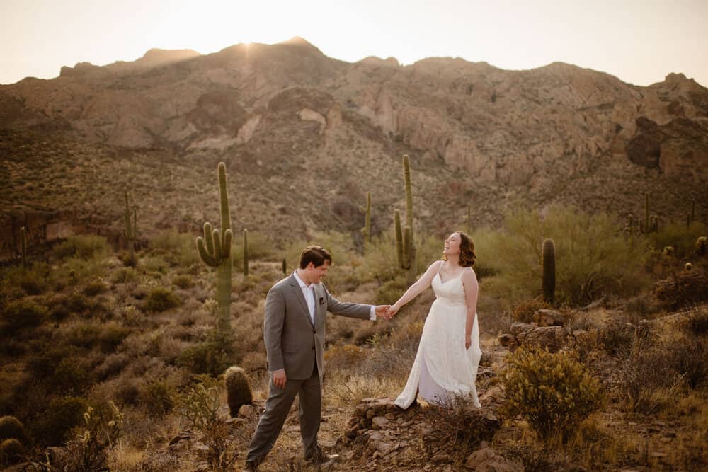 A bride laughs as her groom leads her down the trial in the desert. 