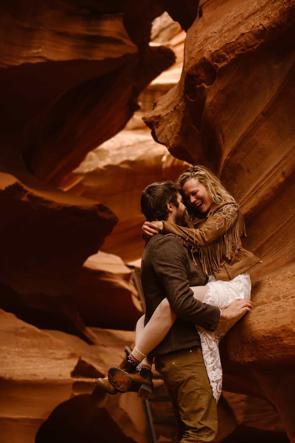 A groom holds his bride agains the slot canyon wallks as she laughs.
