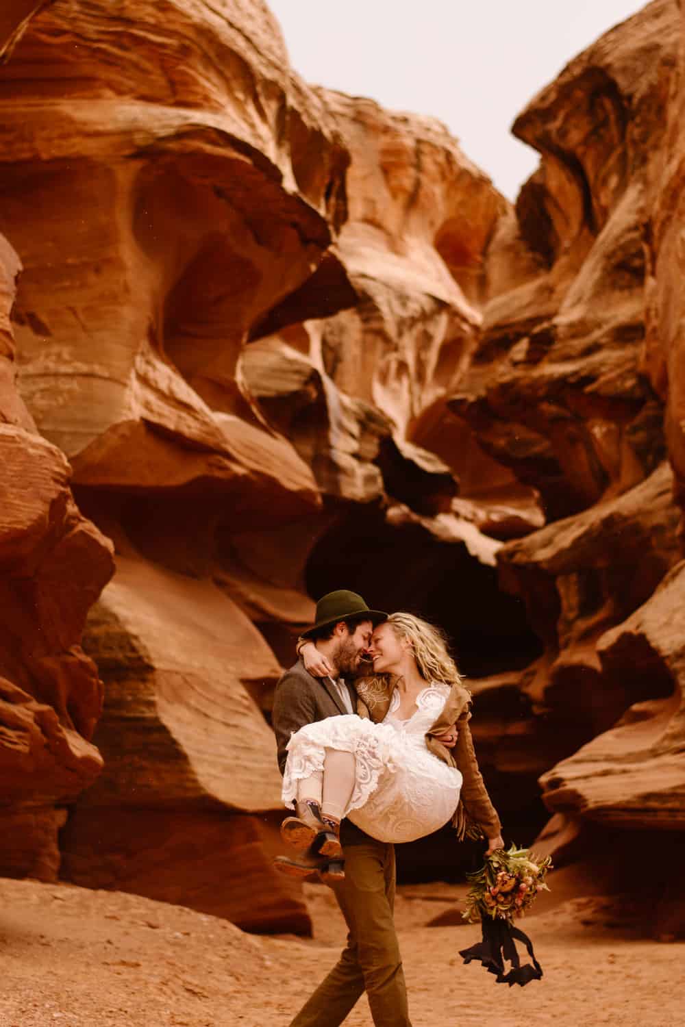A groom scoops up his bride as they smile holding each other in a slot canyon.