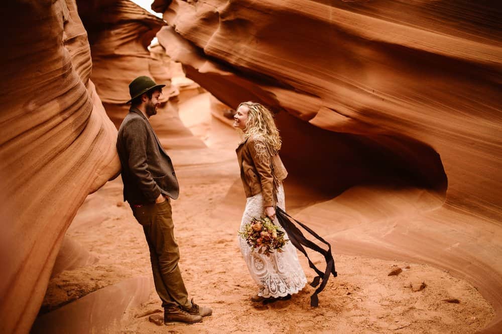 A groom smiles at his bride as she runs towards him in a slot canyon. 