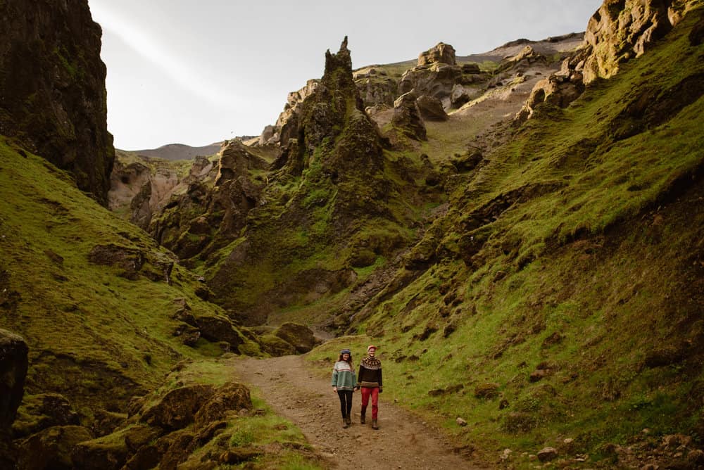 A couple walks together on the trail towards the camera surrounded by mossy canyon walls. 