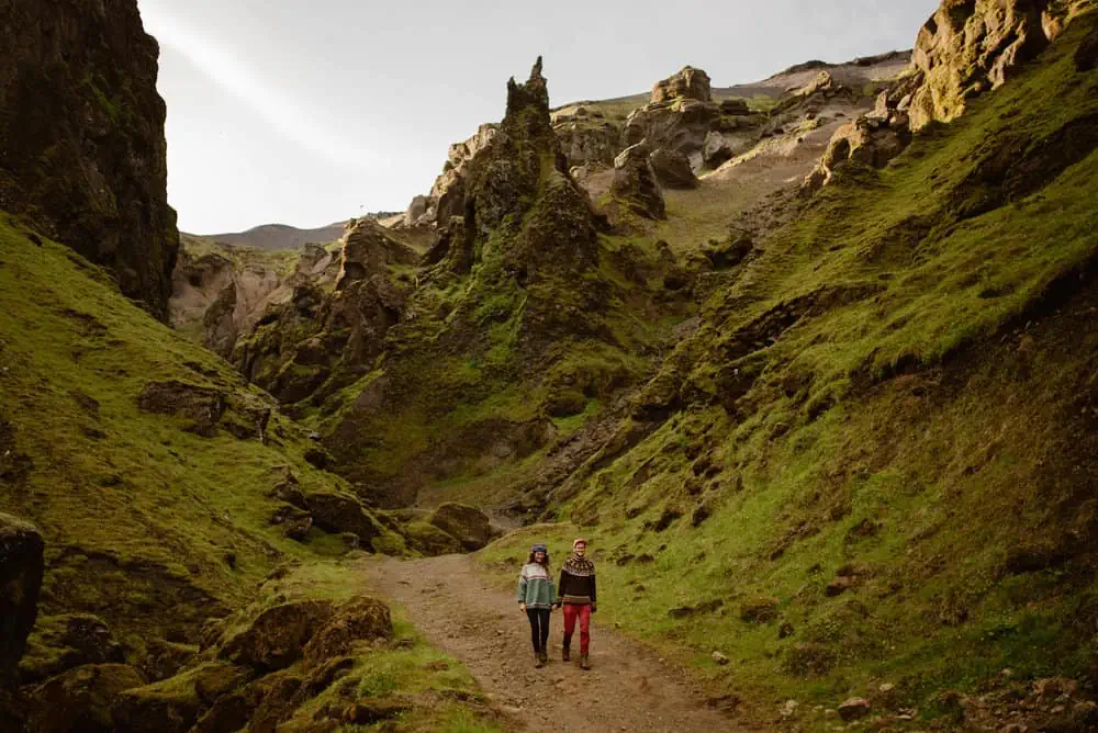 A couple walks together on the trail towards the camera surrounded by mossy canyon walls. 