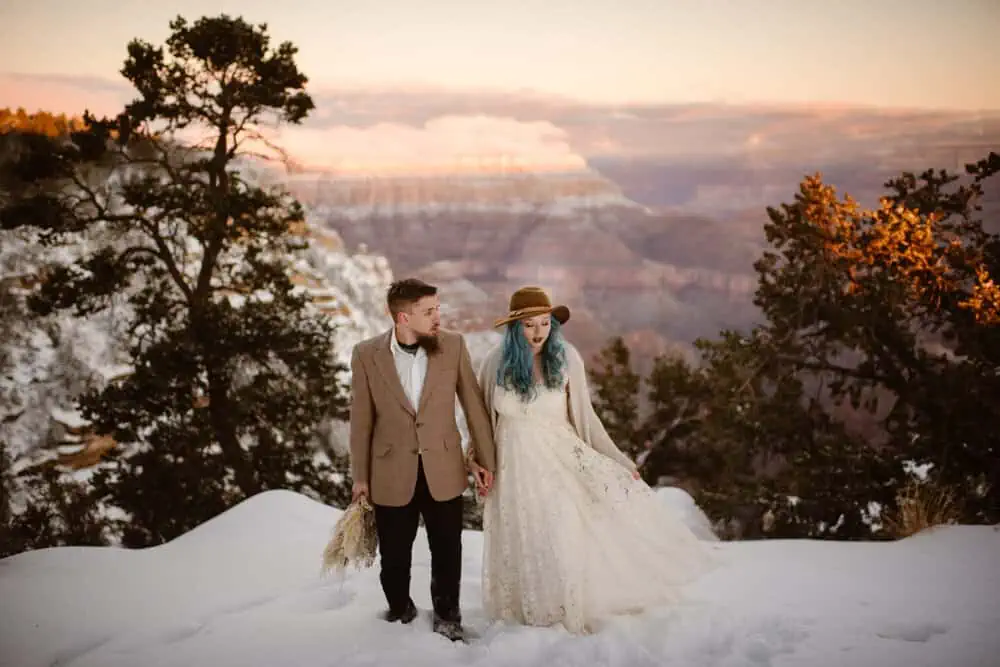 A couple walks around on a snowy vista at sunrise in the Grand Canyon.