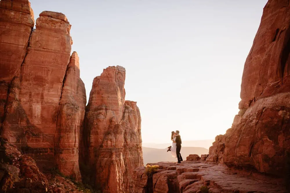 A couple embrace while standing out on the ledge of cathedral rock.