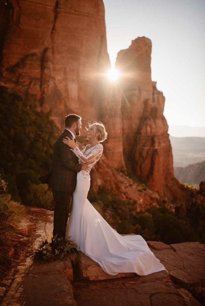 A bride smiles and laughs as her and her husband stand in the sunlight. 