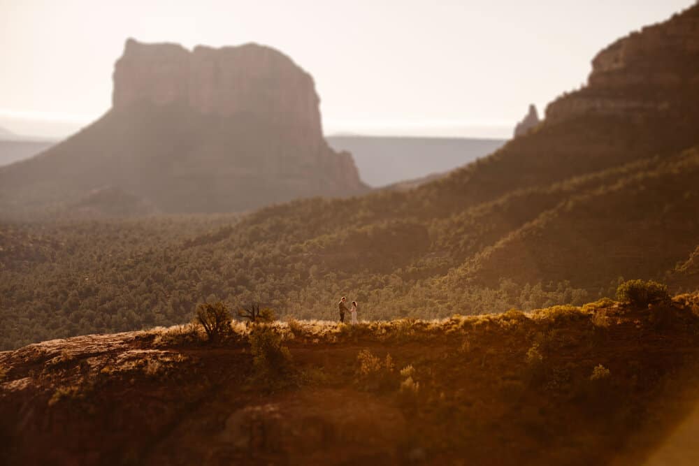 A couple walk together along the red rocks in the morning sunlight in Sedona.