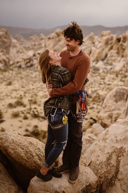 A couple shares a hug in the wind on top of a climbing route. 