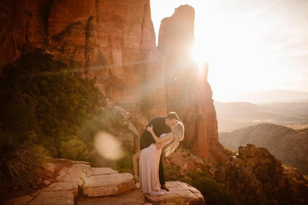 A man kisses his soon to be wife on the top of the red rocks at sunset. 