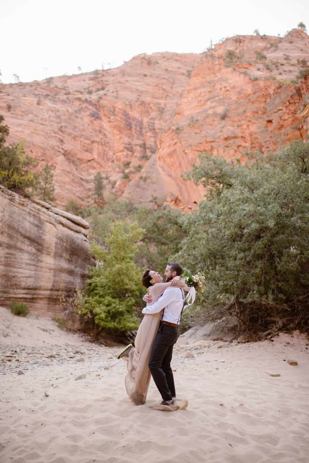 The bride and groom hug each other while smiling and laughing while playing near a slot canyon in Zion National Park.
