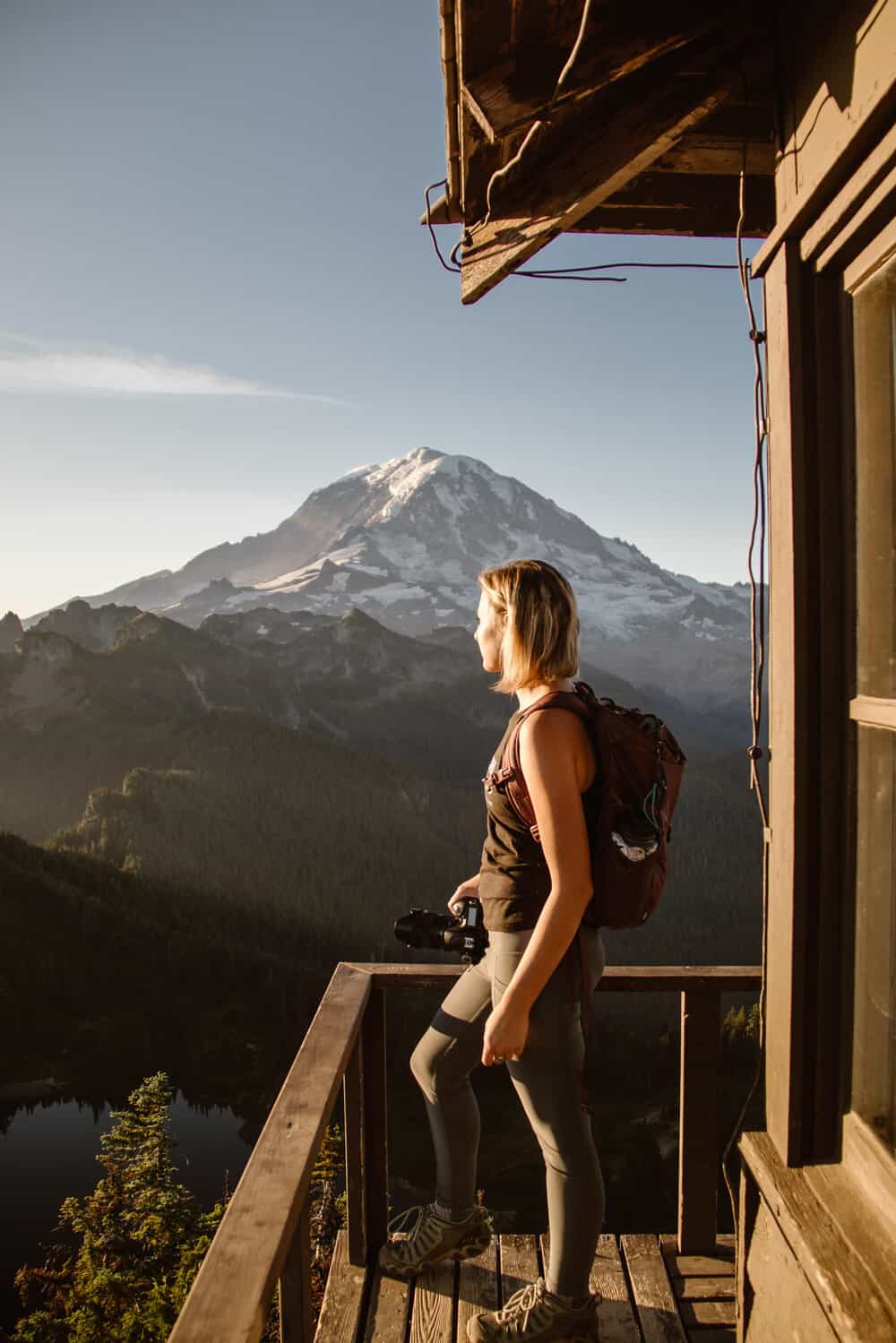 A girl looks out towards mt rainier while standing on the deck of Tolmie peak at sunrise. 