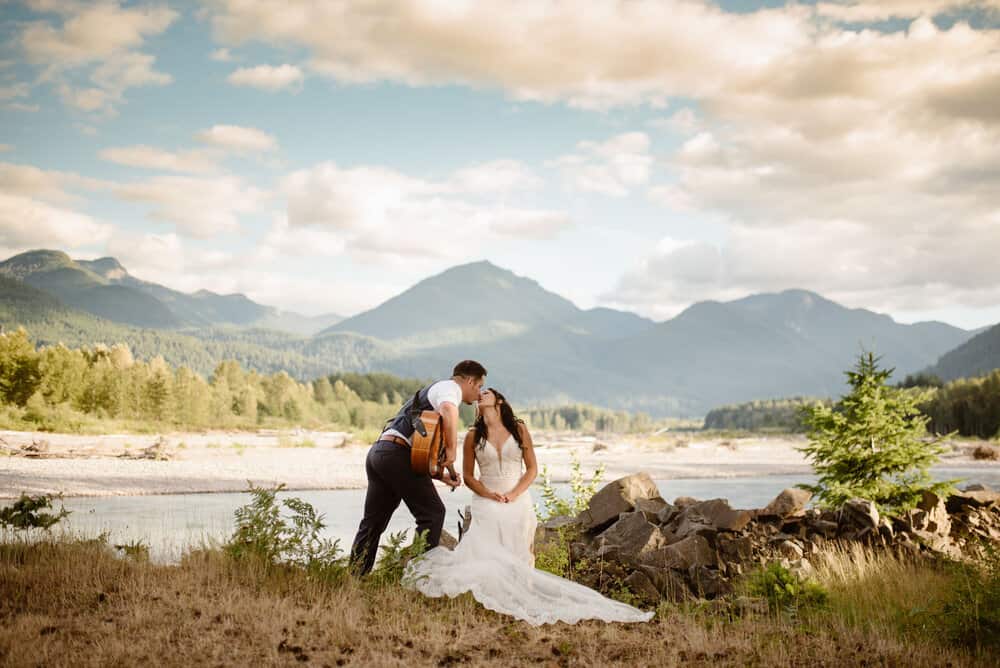 A groom sings a song and plays the guitar for his bride at the river in Packwood.