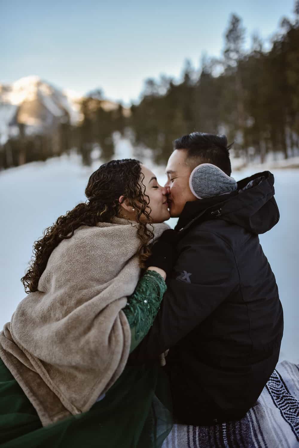 A couple kisses while cuddled up in the snow. 