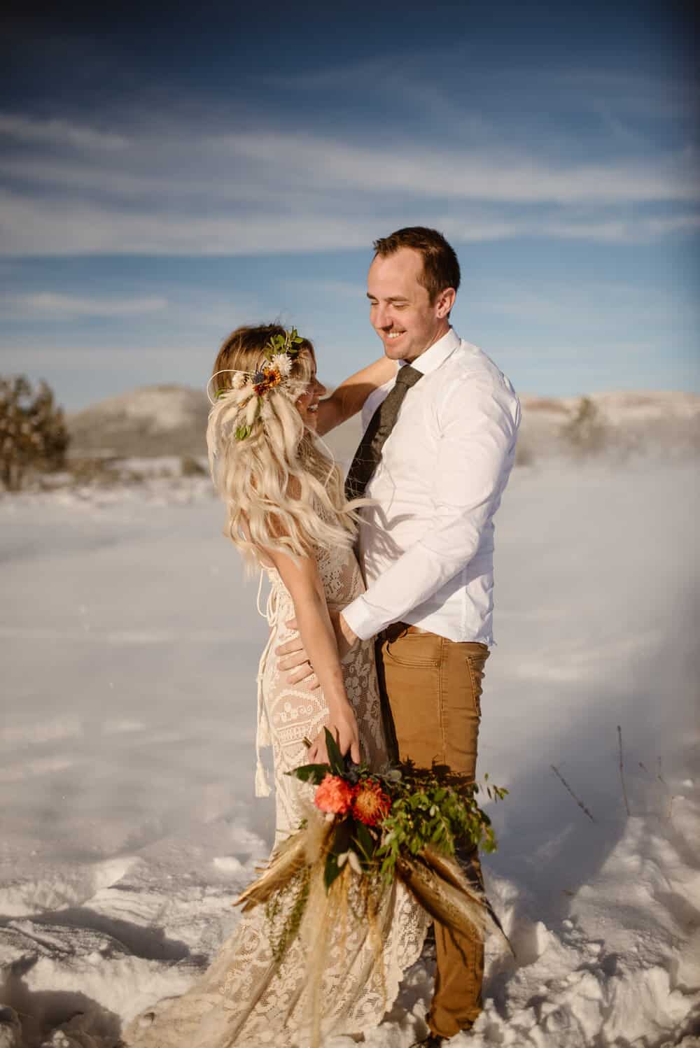 A groom smiles at his bride on a sunny day in the winter. 