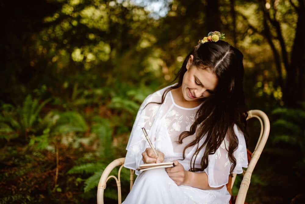 An image of a woman writing in a vow book while wearing her wedding dress.