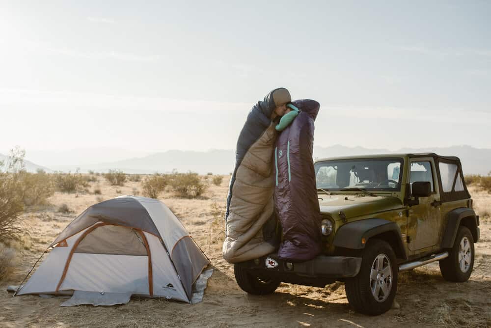 A couple shares a. kiss on the hood of their jeep by their camp site in the desert. 