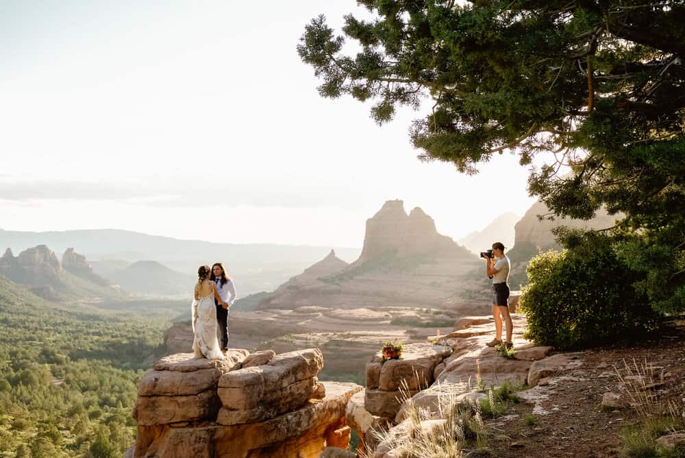 A woman photographs a couple standing on a rock in Sedona.