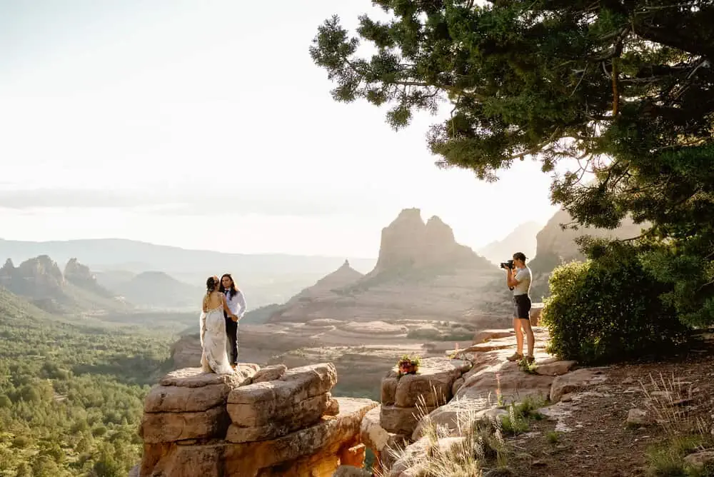A woman photographs a couple standing on a rock in Sedona.