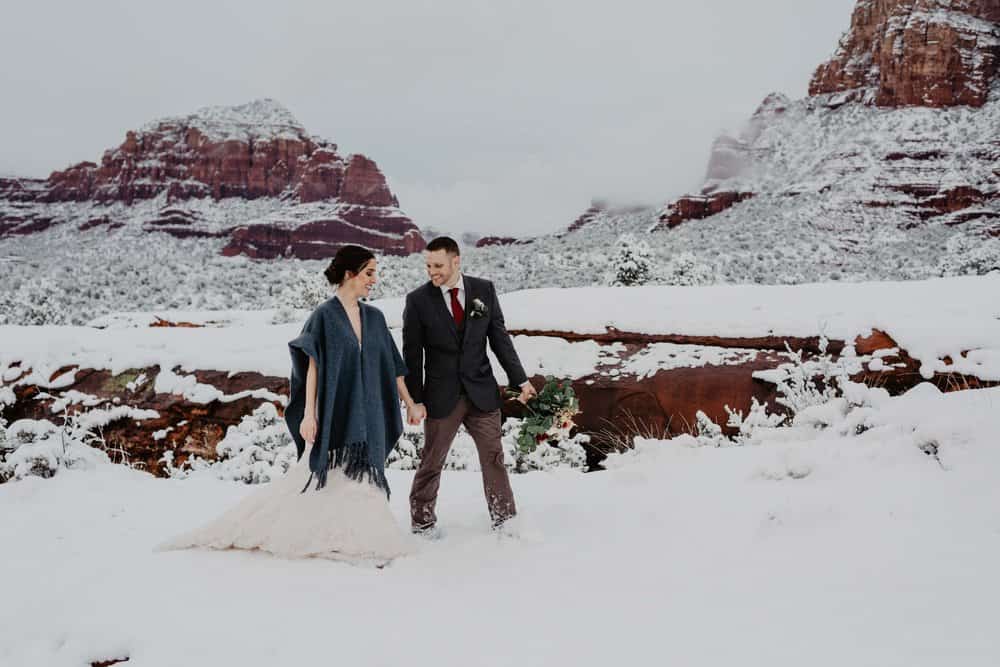 A couple walks through the snow together on a winter day in sedona.