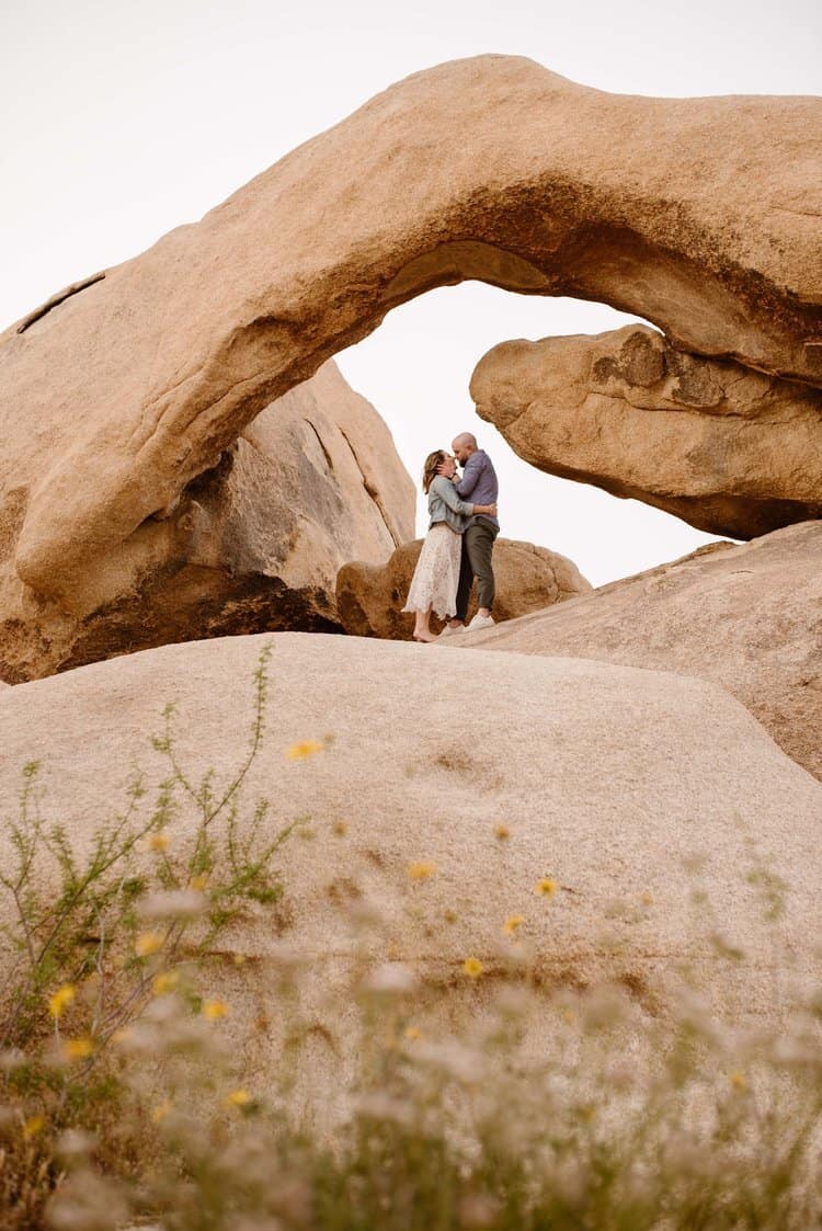 A couple stands under the arch rock in the park.