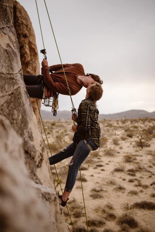 A man kisses his partner as they repel down together on a rock in Joshua Tree.