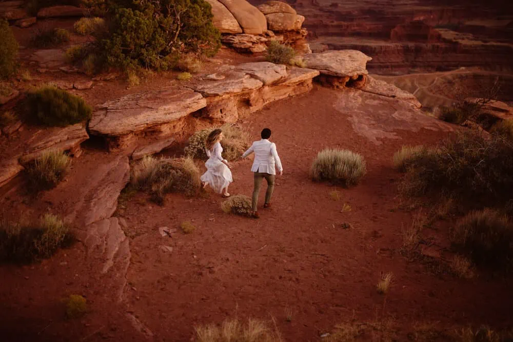 A man and woman run around the desert together int heir wedding attire at blue hour.