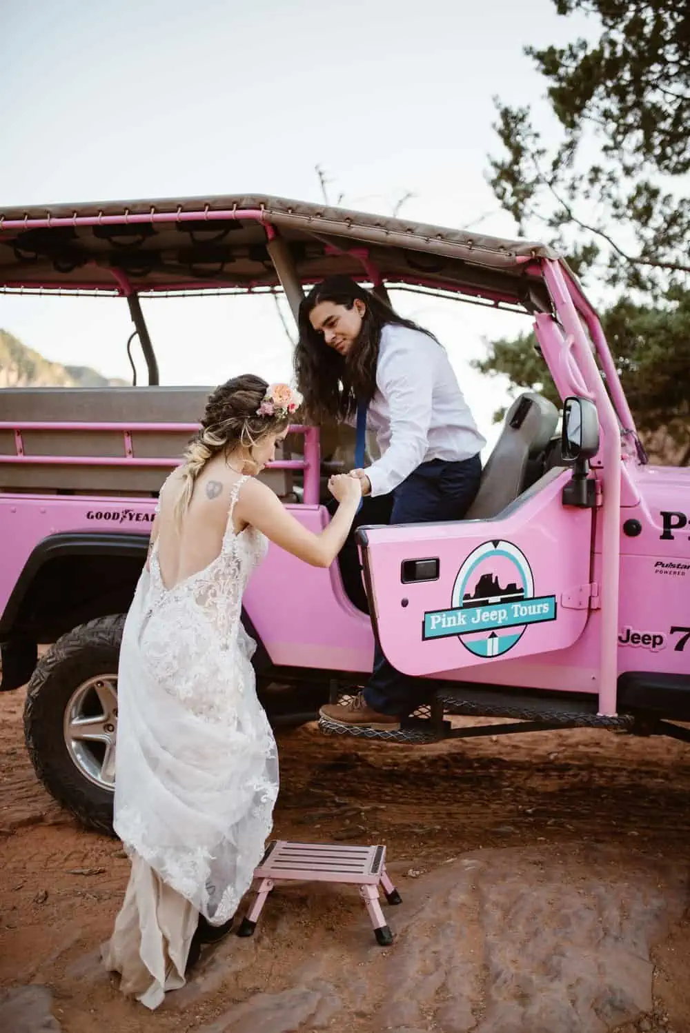 A groom helps his bride into a the jeep.