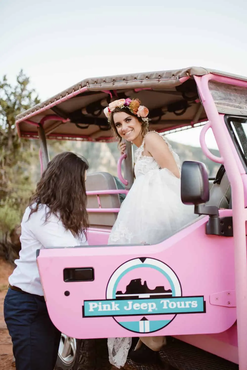 A bride gets out of the jeep while wearing her wedding dress. 