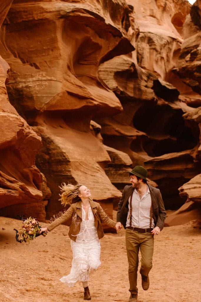 A couple runs together through a slot canyon. 