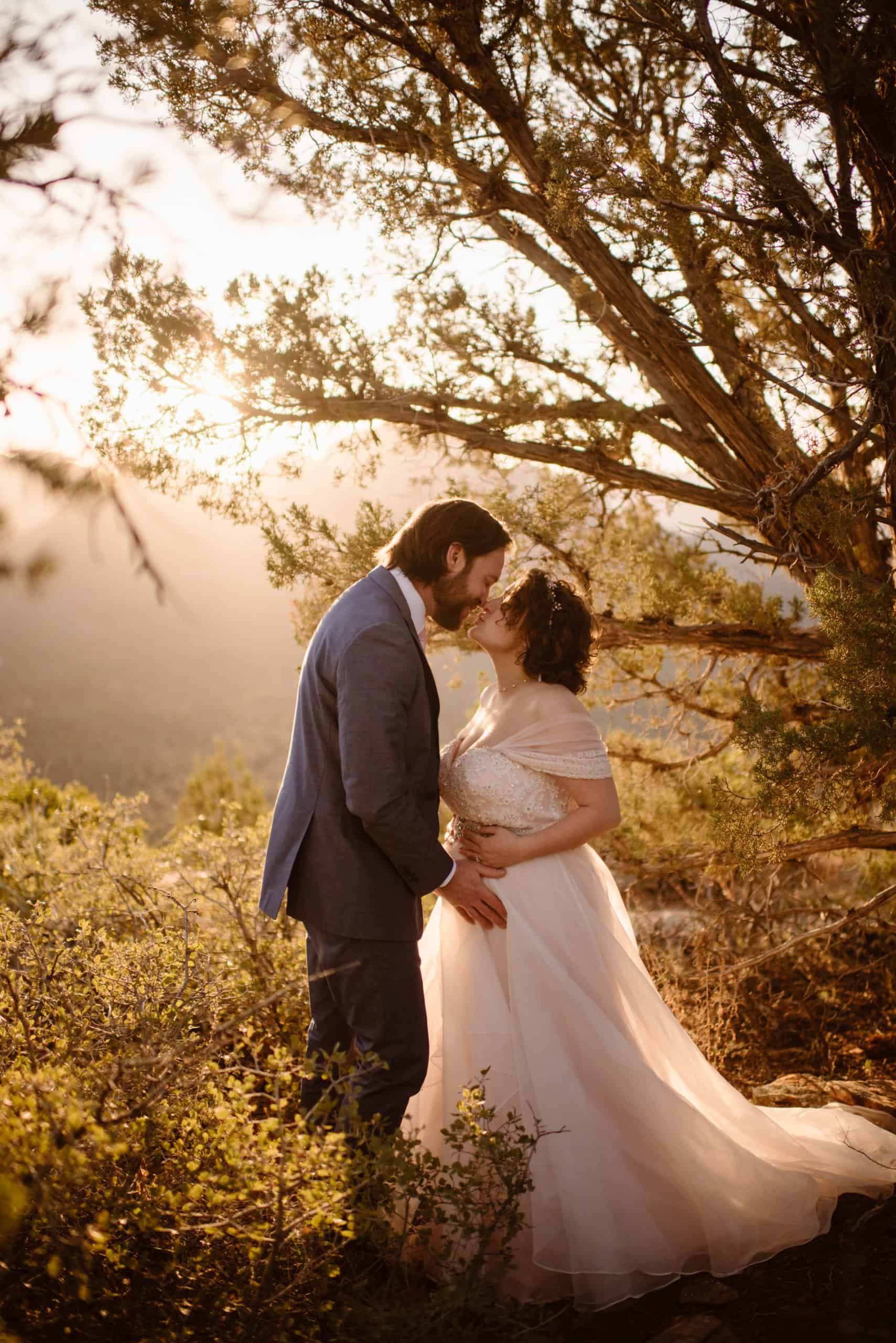 A bride and groom share a kiss among the desert trees of Sedona at sunrise
