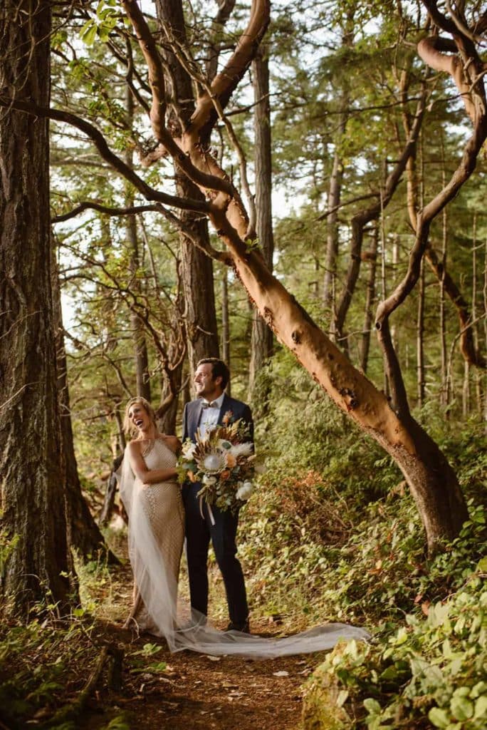 A bride and groom walk together through the forest while they both smile
