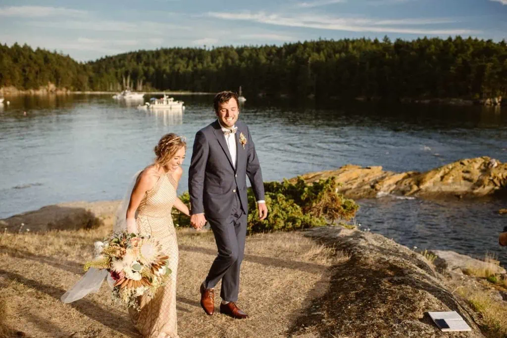 A bride and groom walking hand in hand in celebration of their wedding ceremony on Sucia island.
