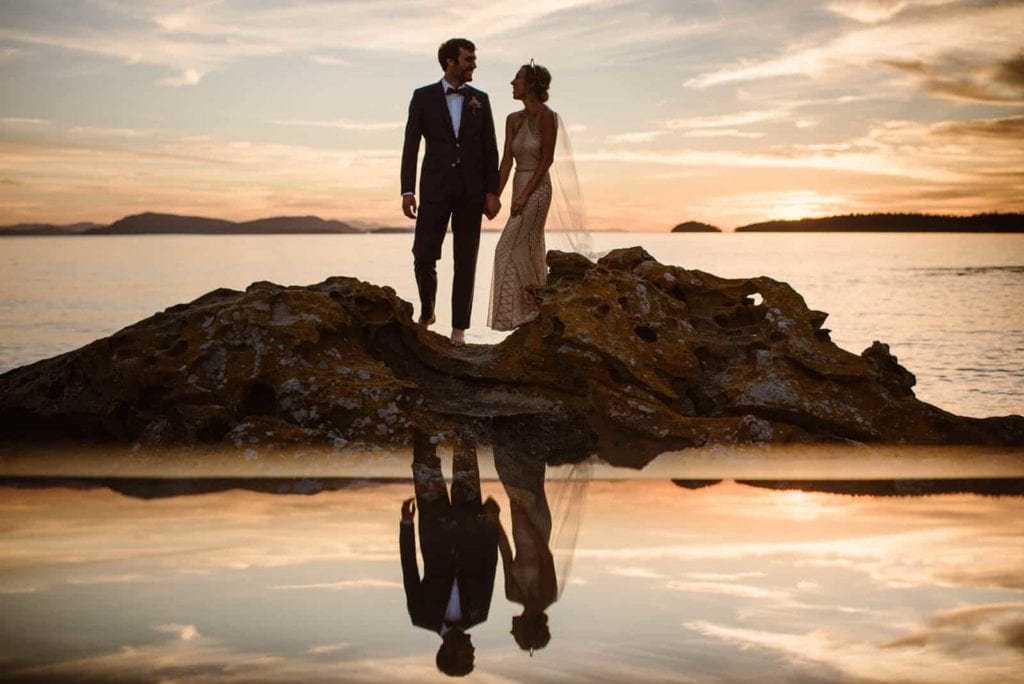 The couple stands together on a rock. 