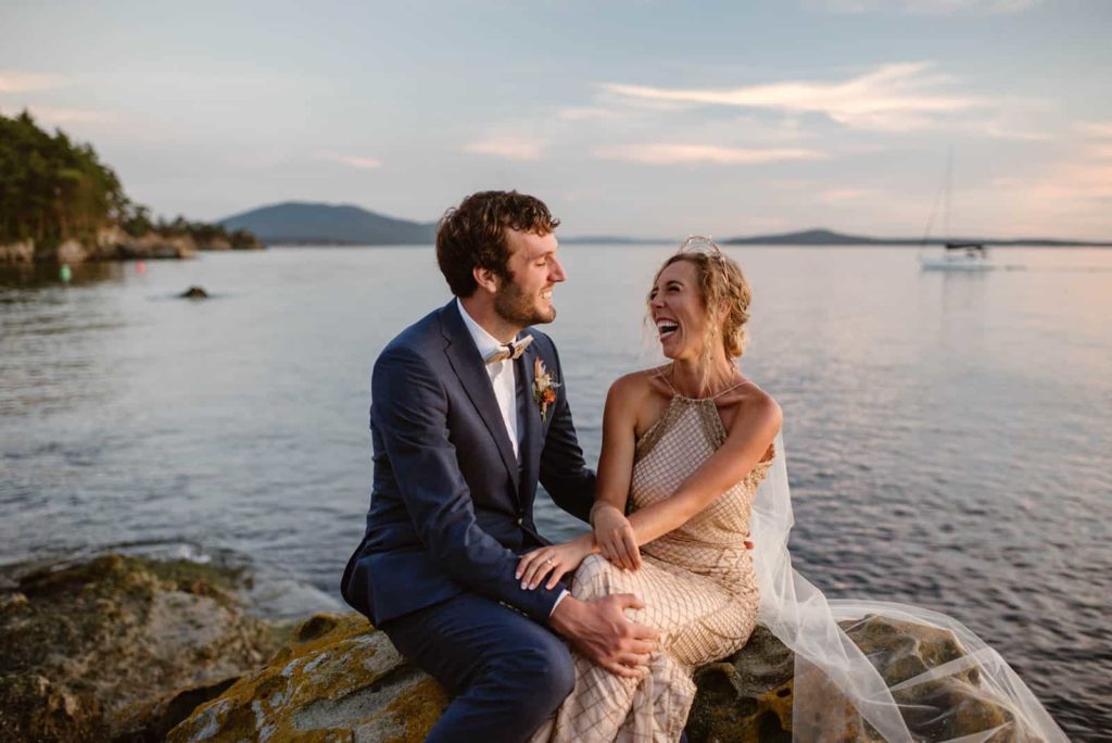 A bride and groom sit together and laugh as the sun finishes setting on Sucia island.