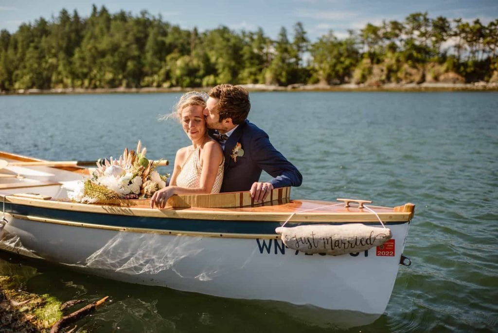 A groom kisses his bride while they sit on their boat together.