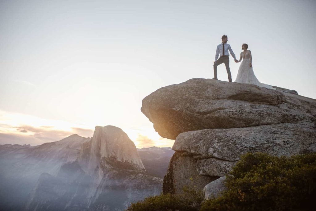 A couple walks along the rocks high in the sky with half dome in the back ground. 