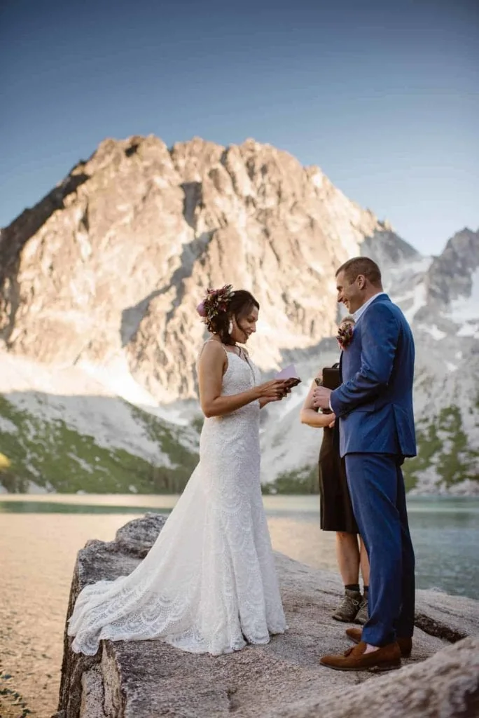 A bride reads her vows to her groom standing in front of Colchuck Lake.