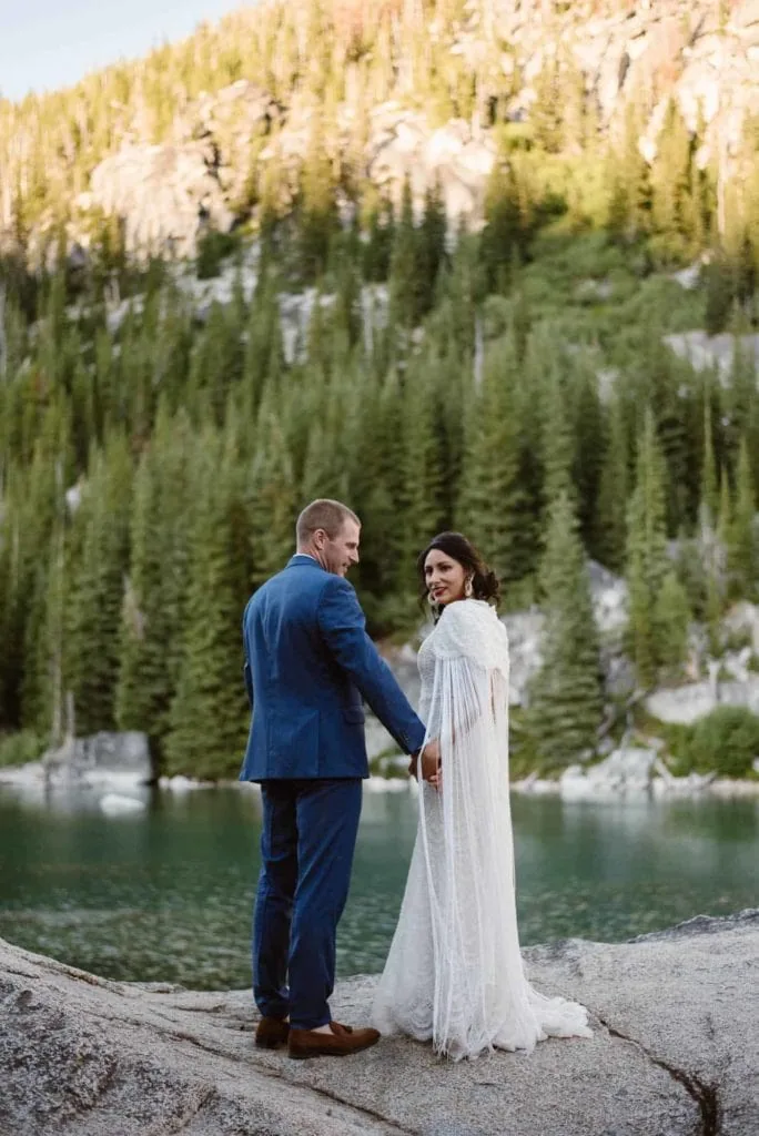 A bride looks back at the camera with a smile with her newly wed husband in the mountains.
