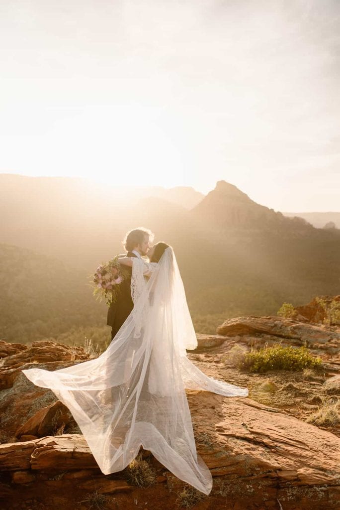 A bride puts her arms around her groom as the sun comes up for sunrise among the red rocks of Sedona.
