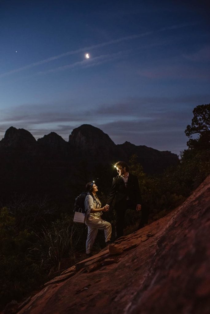 The bride and groom hold hands as they stand together with their headlamps on on their hike to their sunrise ceremony in Sedona.