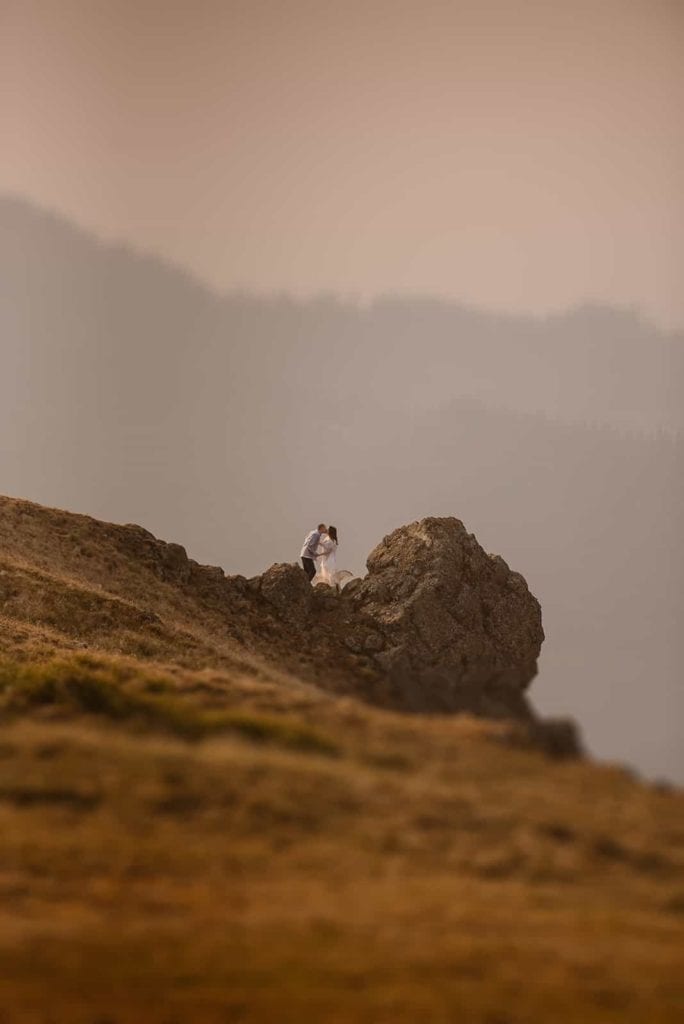 A groom gives his bride a kiss at a distance while they enjoy the sunrise up at Hurricane Ridge.