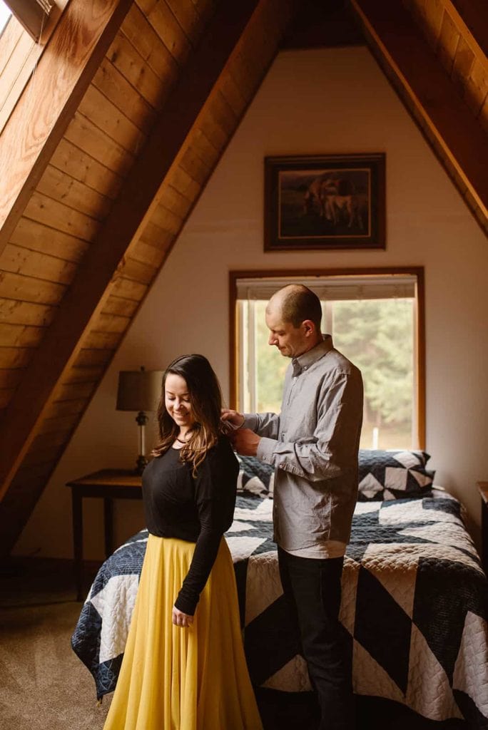 A man helps his wife with her shirt in a cute A frame cabin.